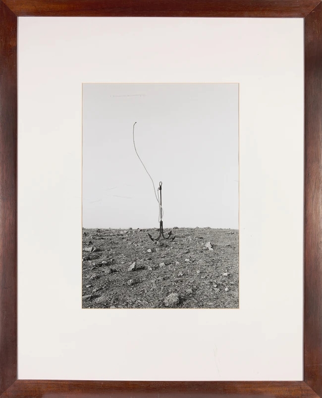 A solitary concrete block floats in a vast, calm sea under a pale sky.