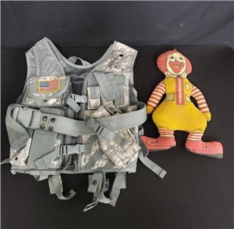 A military-style vest and a clown plush toy sit side by side on a dark surface.