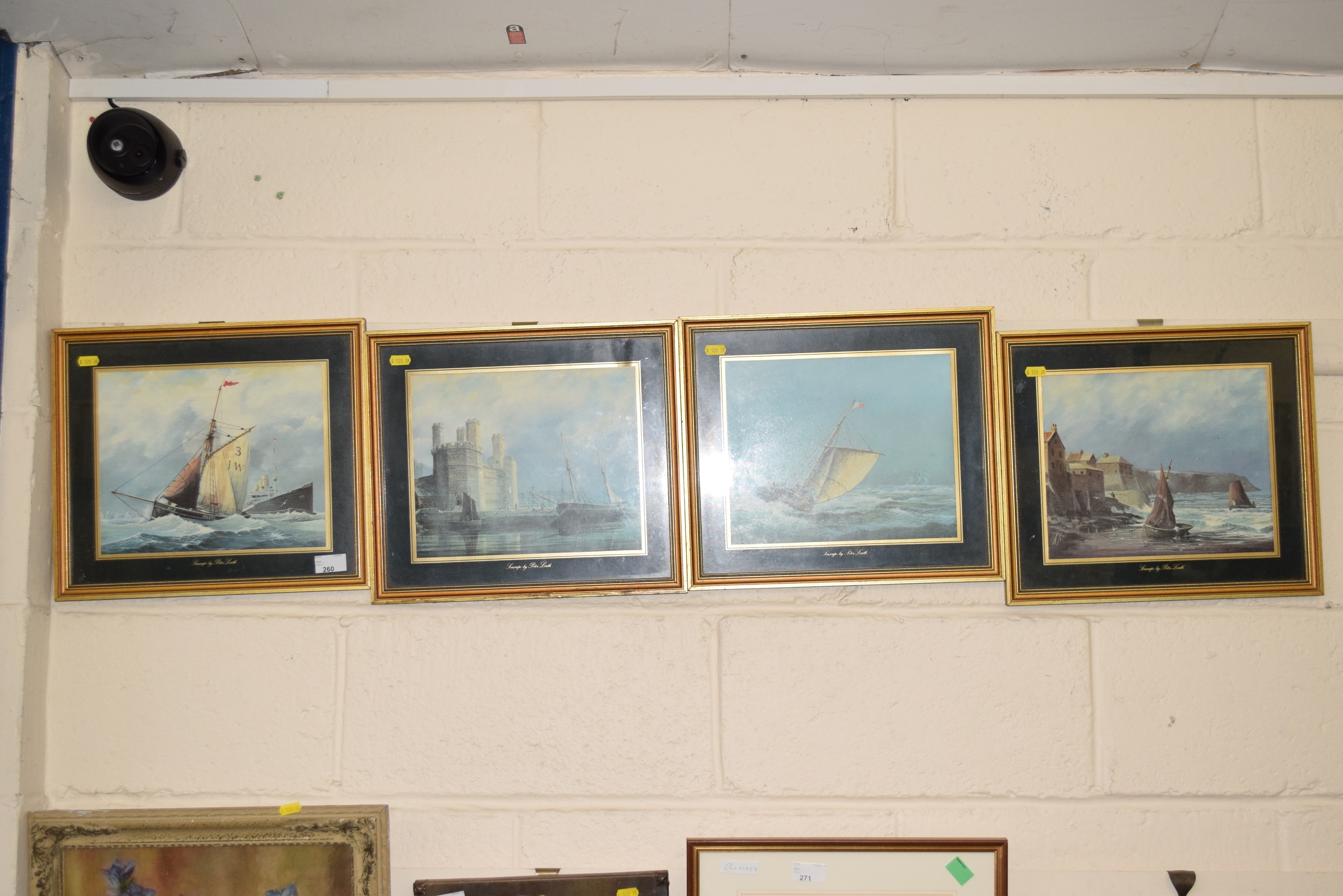 Four framed maritime paintings hang in a row on a white brick wall.