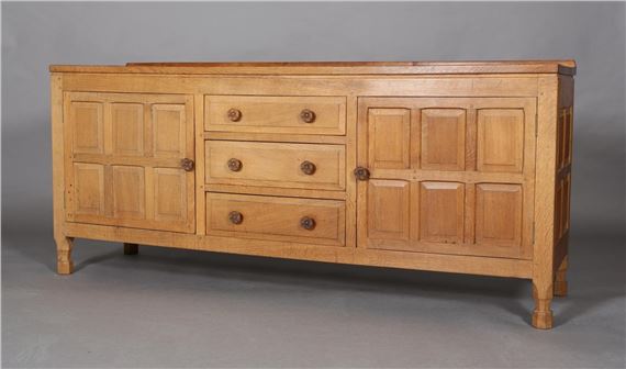 FOX MAN - DON CRAVEN OF LANGTHORPE, BOROUGHBRIDGE, An adzed oak sideboard having a short raised back, three graduated drawers to the centre flanked by a six field-panelled cupboard door to either side, Tudor rose carved handles, on turned stile feet, carved in relief with a fox, 183cm wide x 50cm deep x 78cm high by Don Craven