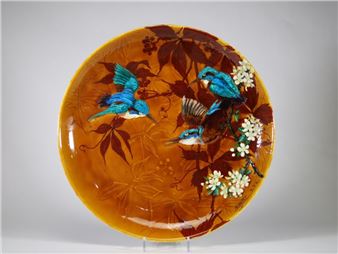 A round ceramic plate featuring a vibrant nature scene with blue birds and white blossoms.