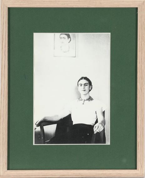 Mexican painter Frida Kahlo (1907–1954) sitting in an armchair under her self-portrait - Lucienne Bloch