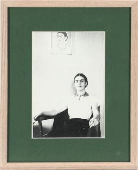 Mexican painter Frida Kahlo (1907–1954) sitting in an armchair under her self-portrait - Lucienne Bloch