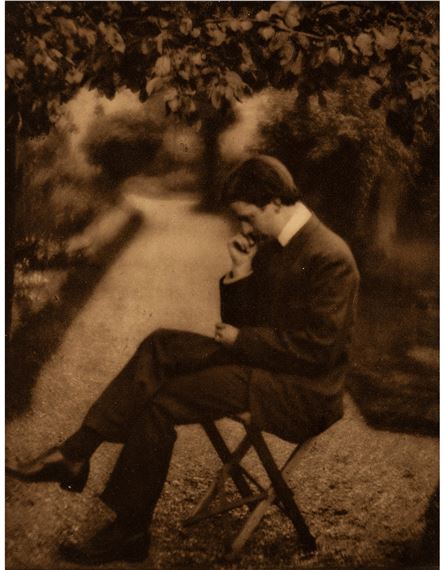 A sepia-toned portrait of a seated figure in an outdoor setting.