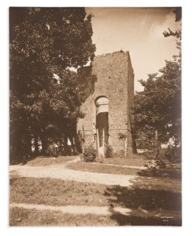 A sepia-toned photograph of a stone ruin with an arched doorway, framed by trees and a dirt path.