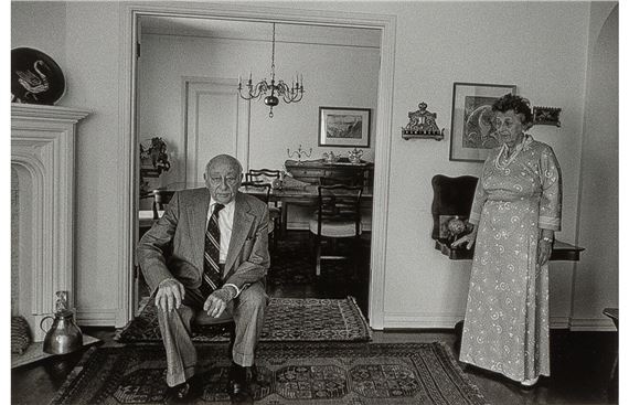 A black-and-white portrait of a seated man and standing woman in a formal interior.