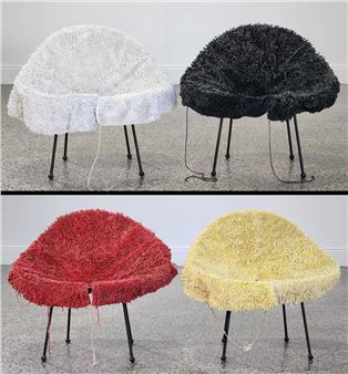 Four plush, shaggy chairs in white, black, red, and yellow sit on a speckled floor against a plain wall.