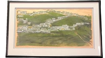 A framed landscape print depicting a hillside town with white buildings nestled among green slopes.