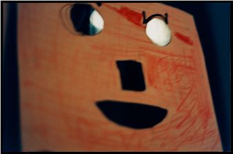 A close-up of a handcrafted wooden mask with painted facial features and cut-out eyes.