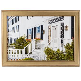 A framed photograph of a white colonial-style house with black shutters and a white picket fence.