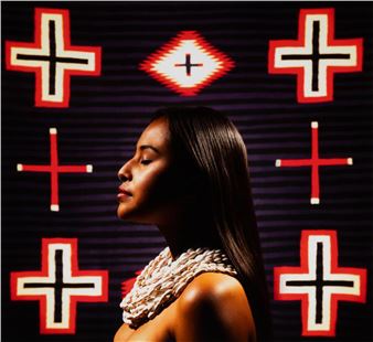 A portrait of a person in profile against a patterned background with red crosses and geometric shapes.