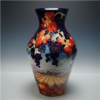 A ceramic vase featuring a vibrant, multi-layered design of autumn leaves, grape clusters, and a pastoral landscape.