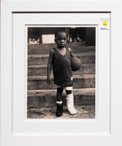 A black and white portrait of a young figure holding a ball, standing on steps with one leg in a cast.