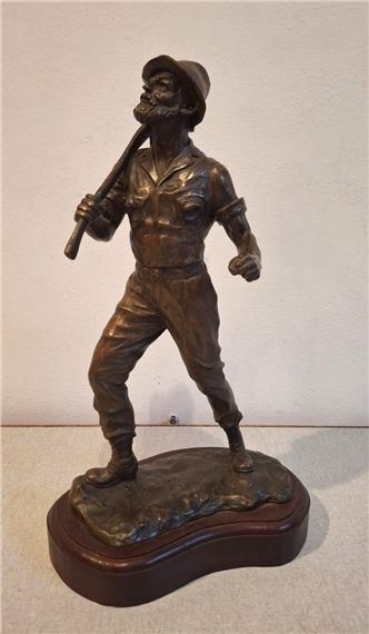 A bronze sculpture of a bearded figure in work clothes carrying a tool over his shoulder.