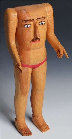 A stylized wooden figure with a blocky head and expressive face, wearing a red loincloth.