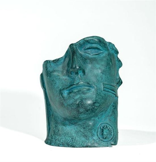 A bronze sculpture of a reclining face with a green patina, resting on a white background.
