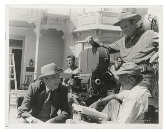 A black-and-white film set scene featuring a crew gathered around a vintage movie camera.