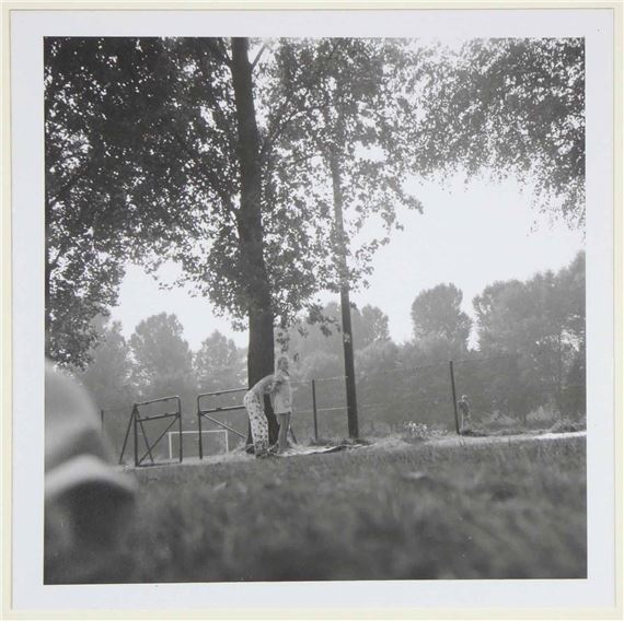 A black-and-white photograph capturing a candid moment of two figures interacting near a tree in an outdoor setting.