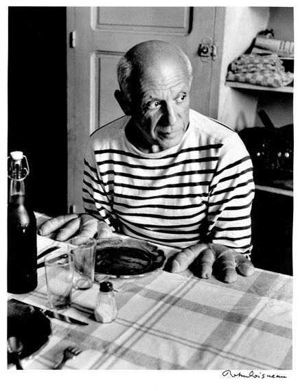 A black-and-white portrait of a seated figure in a striped shirt, gazing off-camera with a contemplative expression.