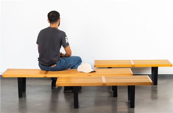 A minimalist interior scene featuring a seated figure and modern benches.