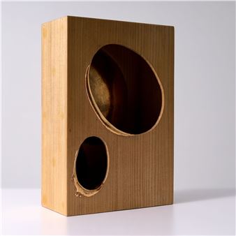A minimalist sculpture featuring a light-colored wooden box with two circular cutouts.