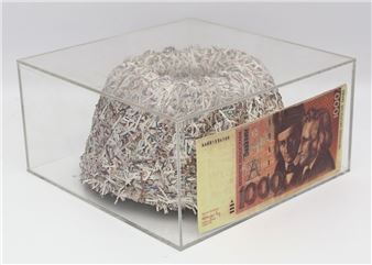 A shredded paper sculpture sits inside a clear box next to a large banknote.