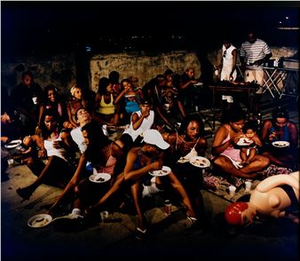 A candid night scene of a group of people eating outdoors with a mannequin in the foreground.