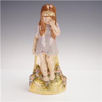 A porcelain figurine of a girl with long hair, wearing a dress and a checkered headband, standing on a floral base.