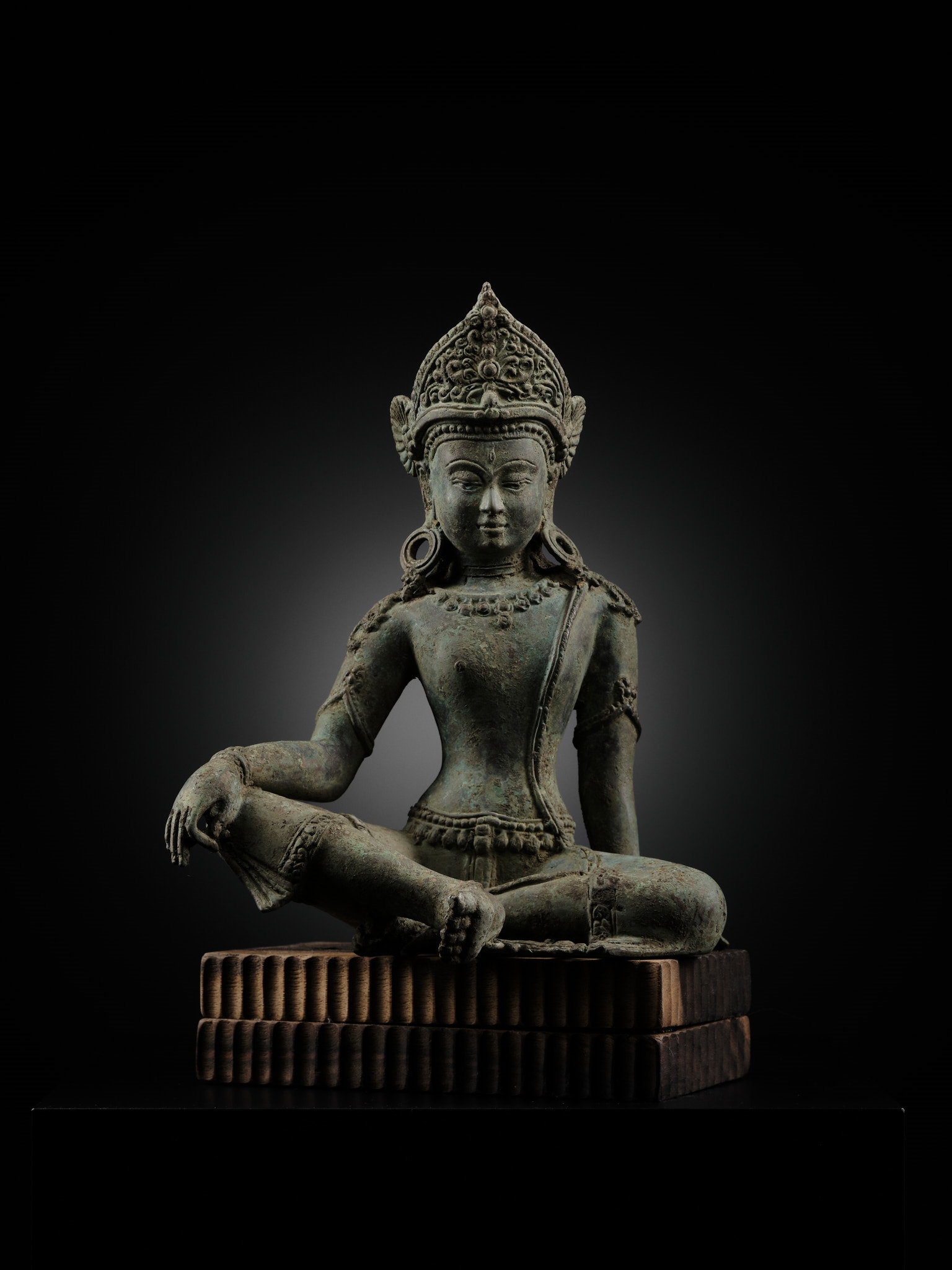 A statue of a seated buddha sitting on a wooden block.