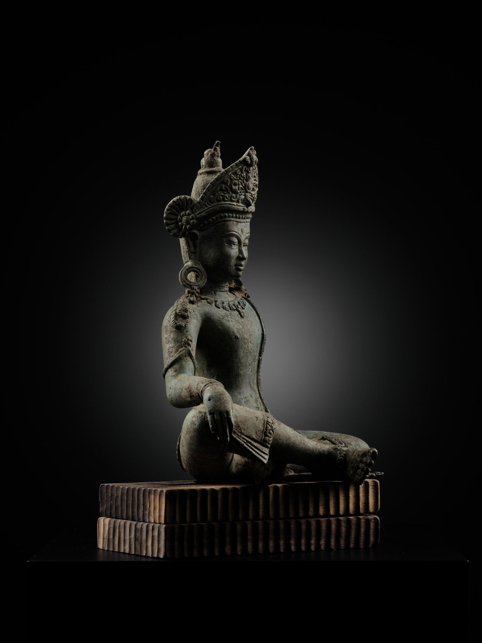 A statue of a seated buddha sitting on a wooden block.