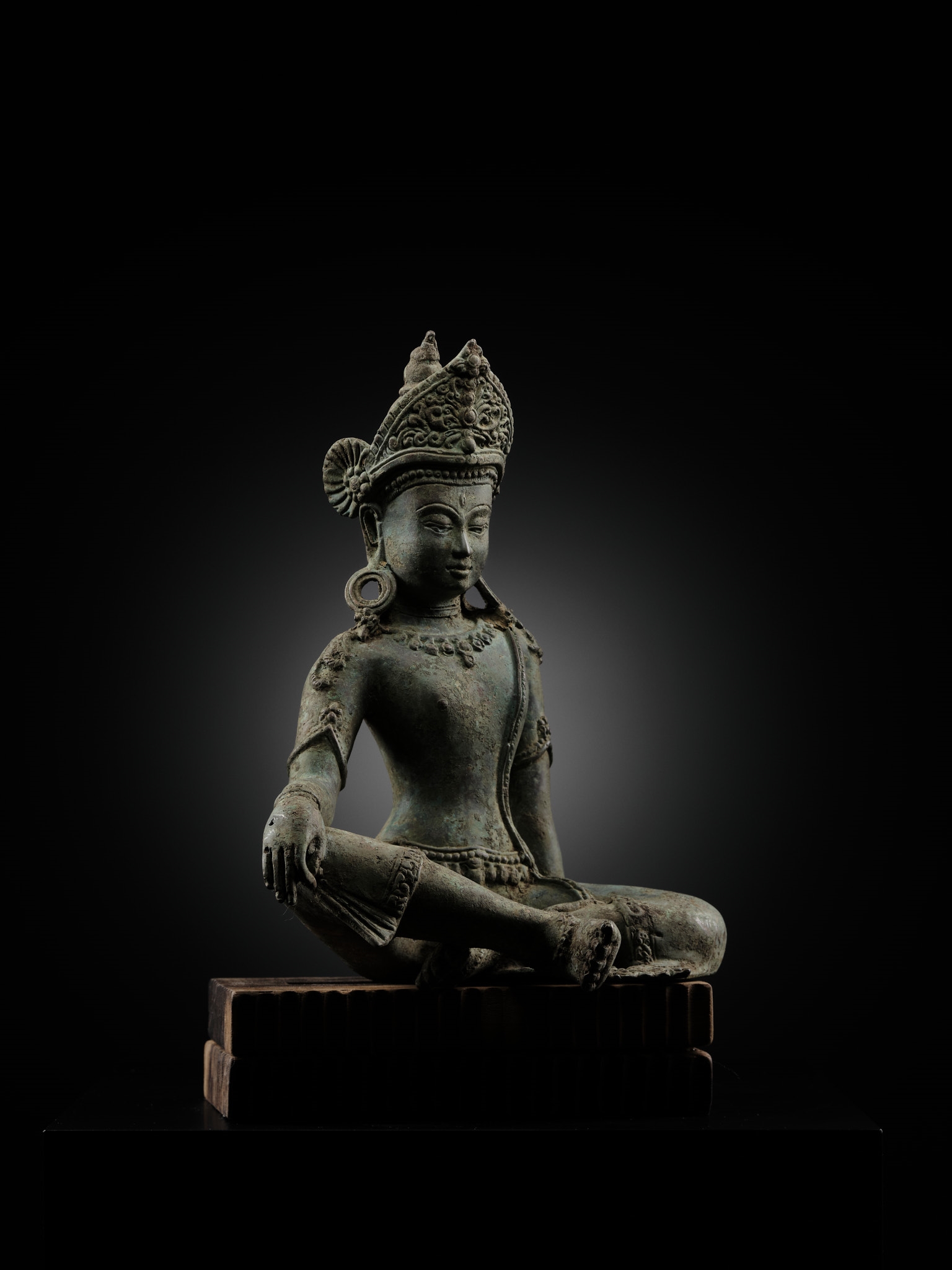 A statue of a seated buddha sitting on a wooden block.