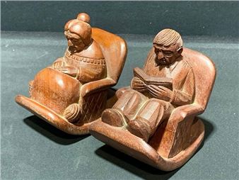 A pair of wooden rocking chair figures carved in a folk art style, depicting an elderly figure and a person reading.