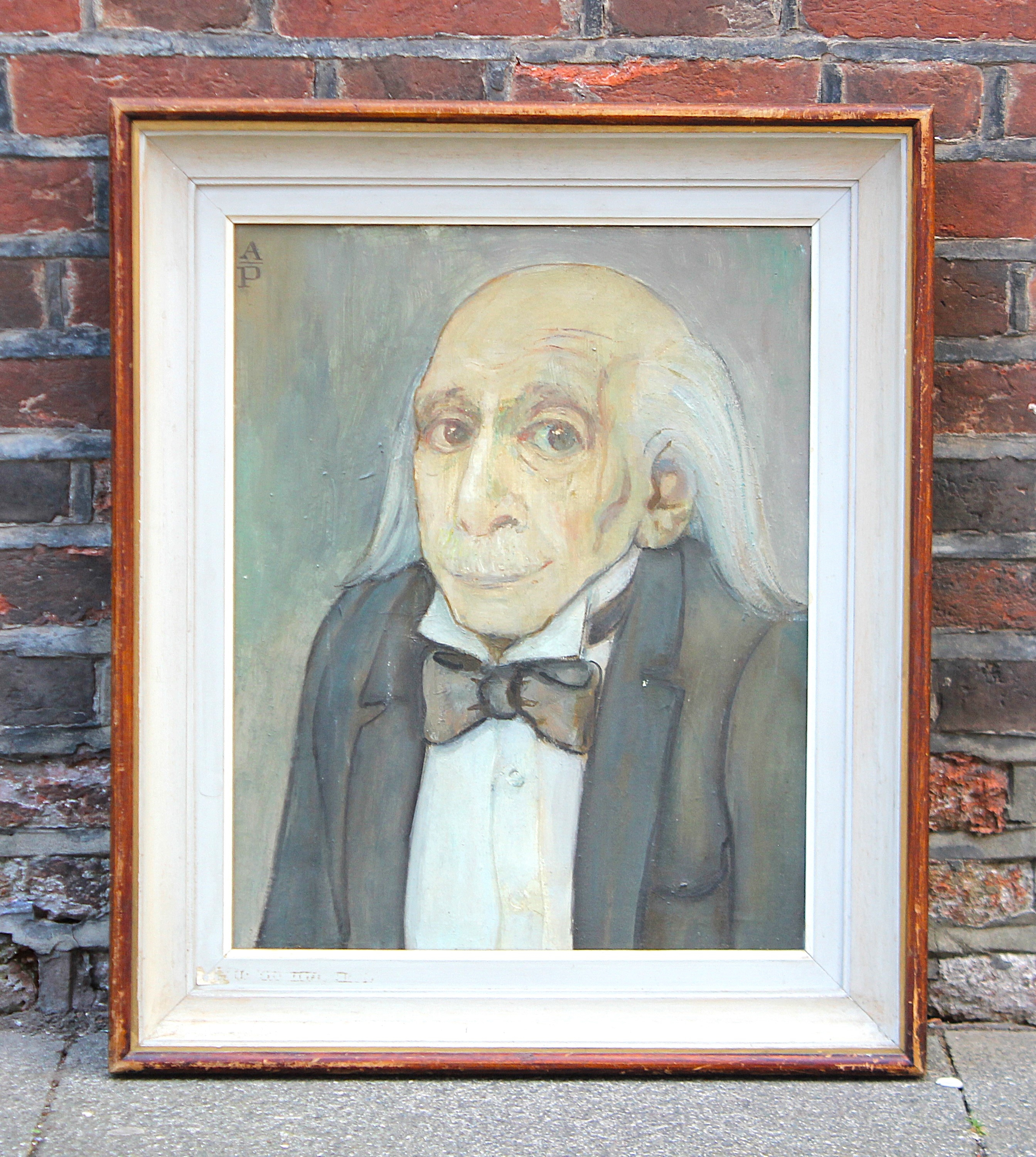 A framed portrait of an elderly man with a bow tie against a brick wall.