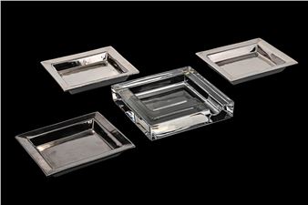 A set of four square silver plates on a black background.