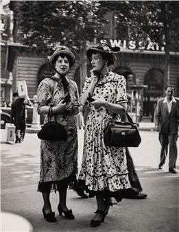 Two women walking down the street talking on their cell phones.