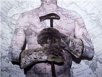 A surreal composition featuring a torso printed with a map, holding a hammer and fur-covered gloves.