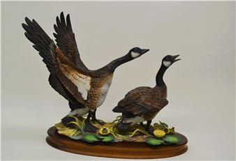 A sculptural diorama featuring two geese in flight and standing poses on a lily pad base.