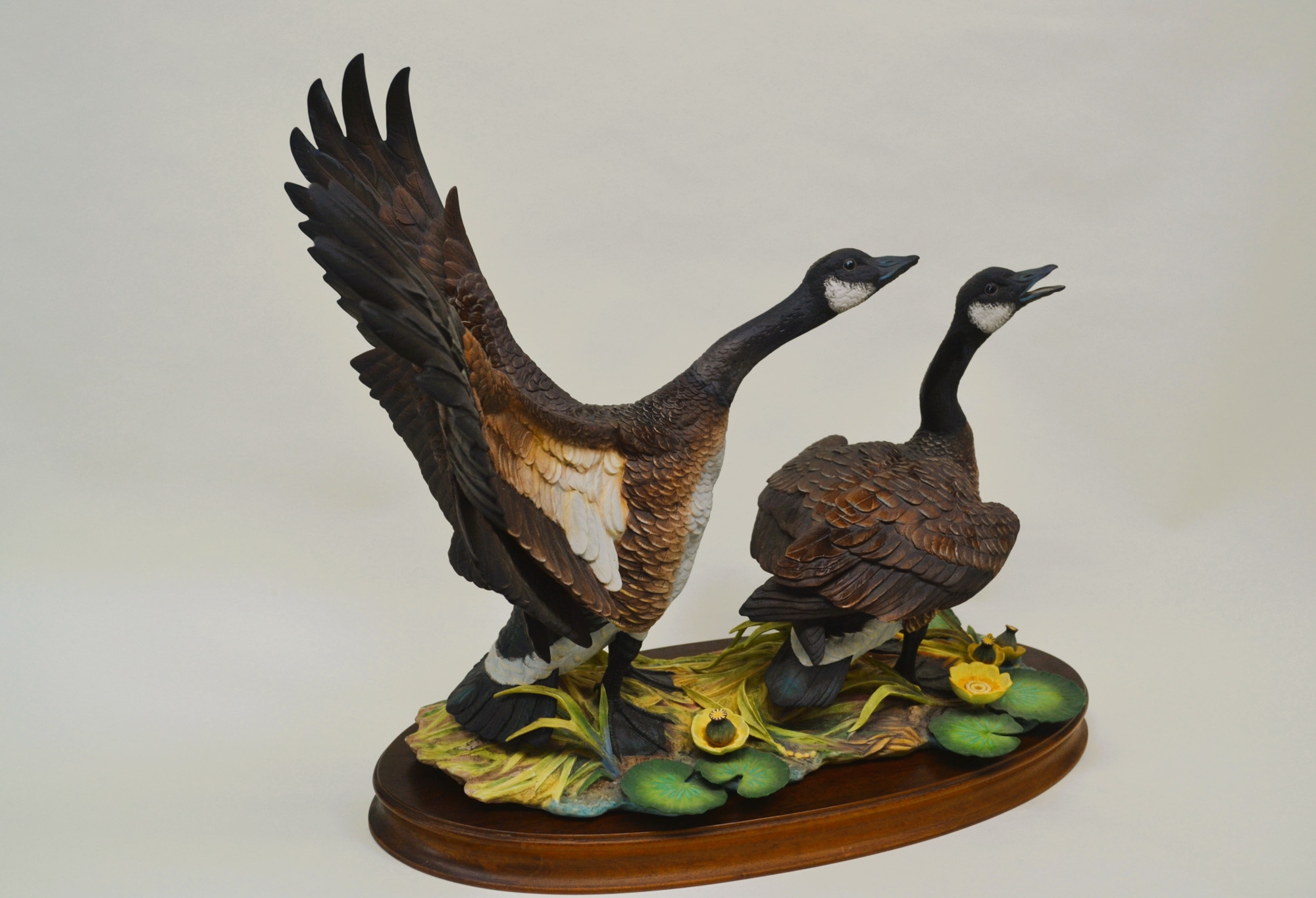 A sculptural diorama featuring two geese in flight and standing poses on a lily pad base.