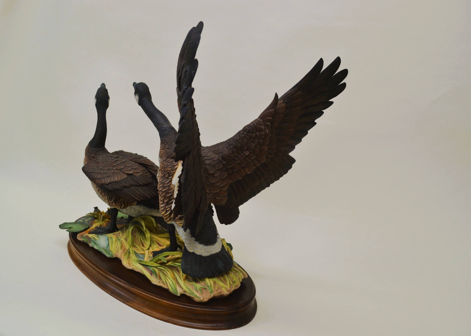 A sculptural diorama featuring two geese in flight and standing poses on a lily pad base.