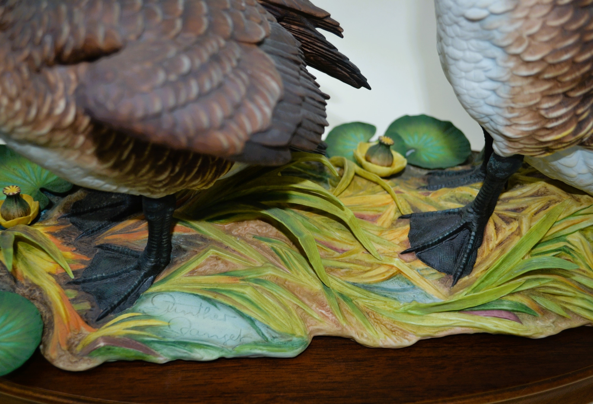 A sculptural diorama featuring two geese in flight and standing poses on a lily pad base.