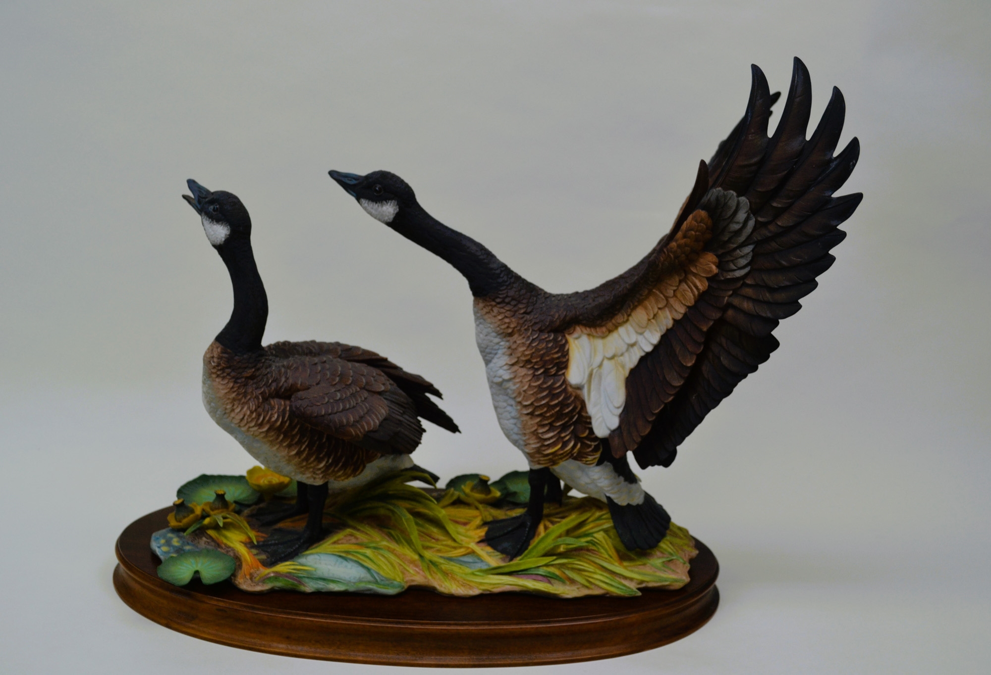A sculptural diorama featuring two geese in flight and standing poses on a lily pad base.