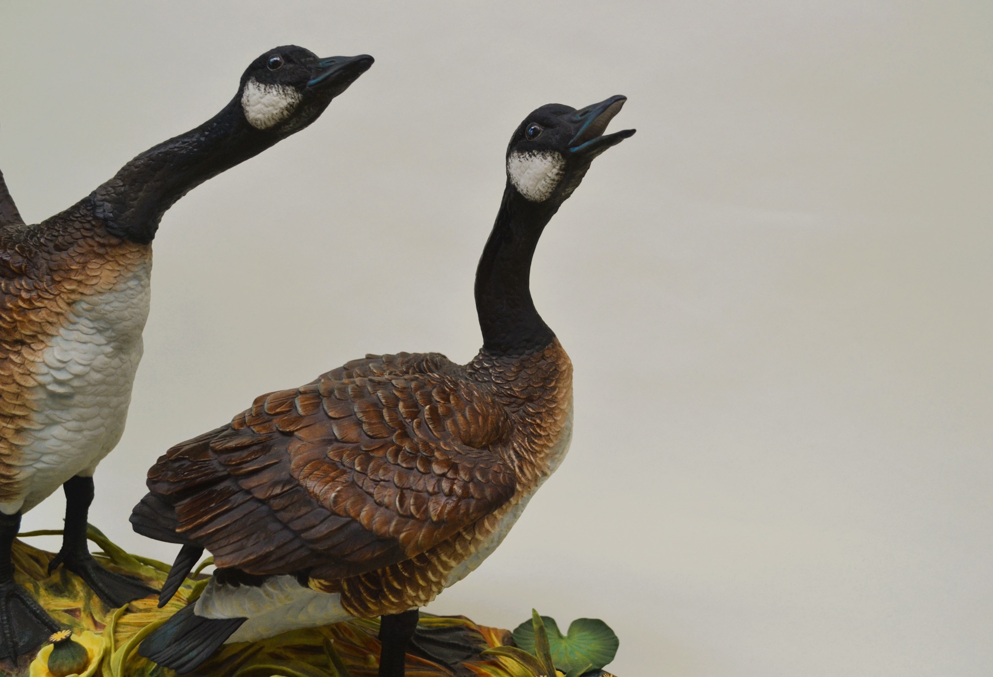 A sculptural diorama featuring two geese in flight and standing poses on a lily pad base.