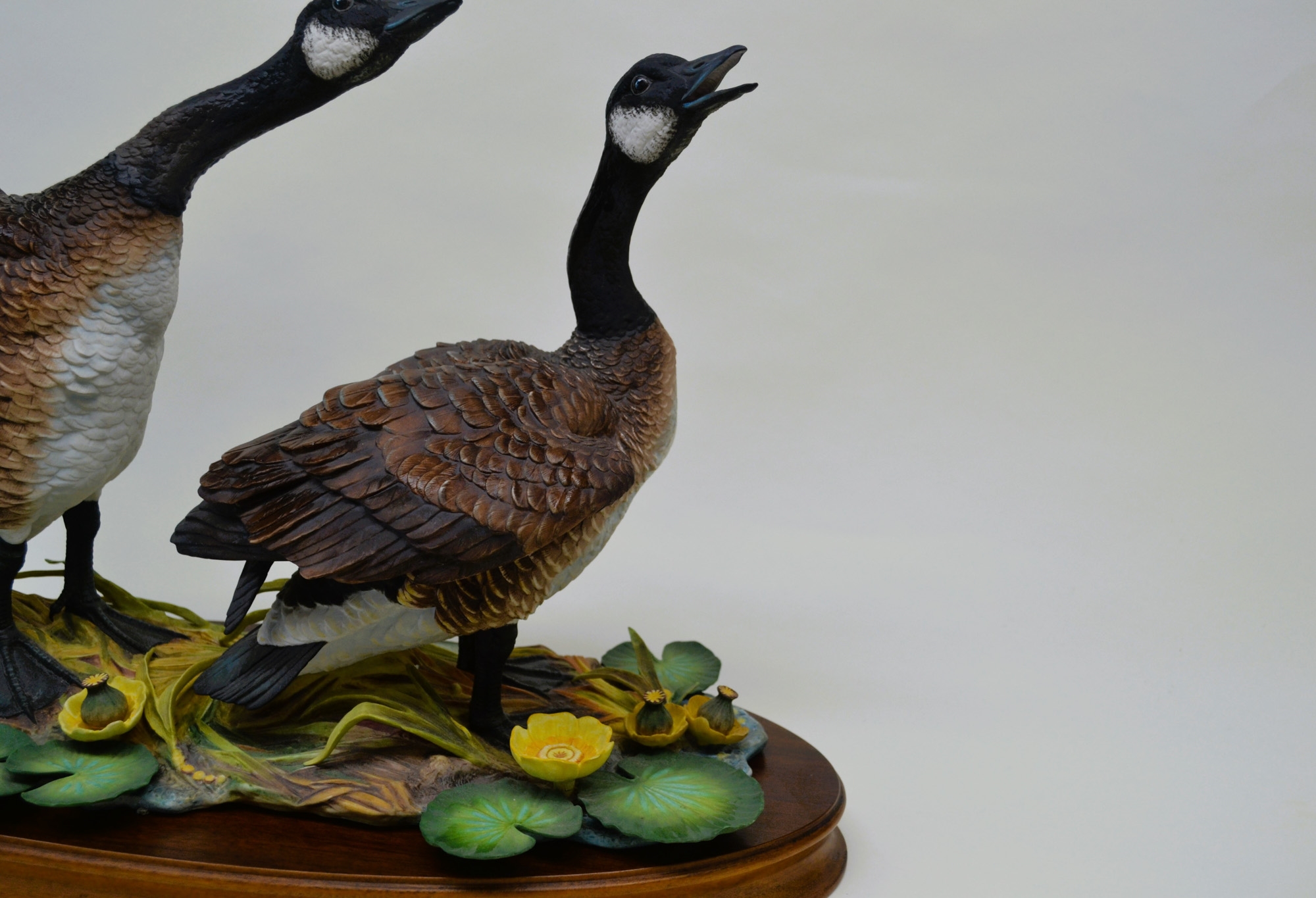 A sculptural diorama featuring two geese in flight and standing poses on a lily pad base.