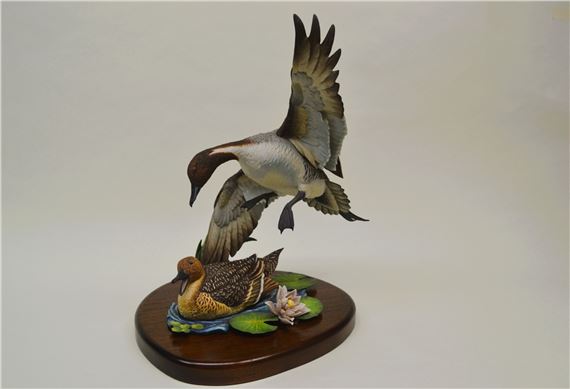 "A sculptural diorama of a bird in flight above a resting duck on a lily pad."