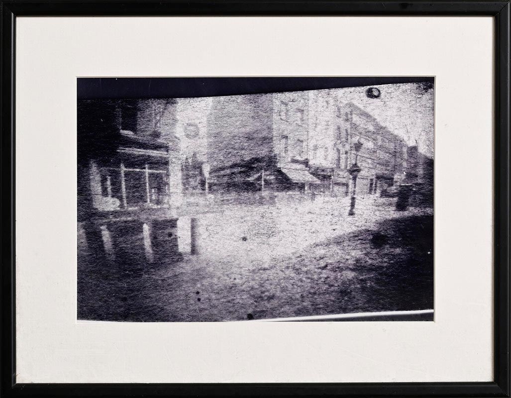A grainy black-and-white street scene with buildings and storefronts.