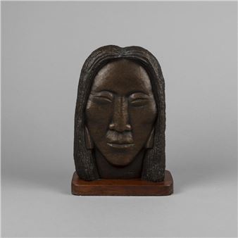 A dark wooden sculpture of a face with long hair resting on a rectangular base.
