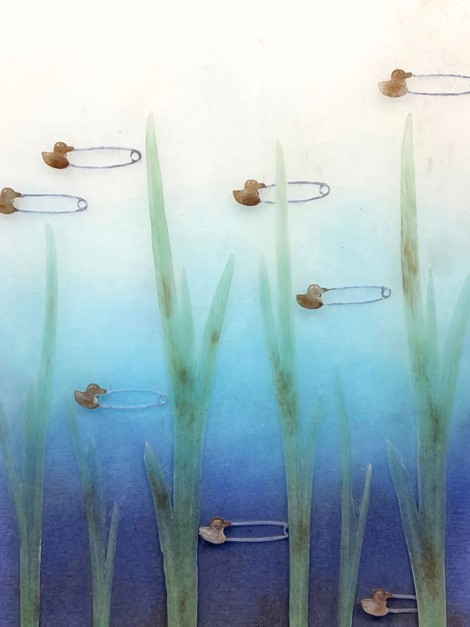 A vertical mixed-media artwork featuring tall green blades and scattered safety pins against a blue gradient background.