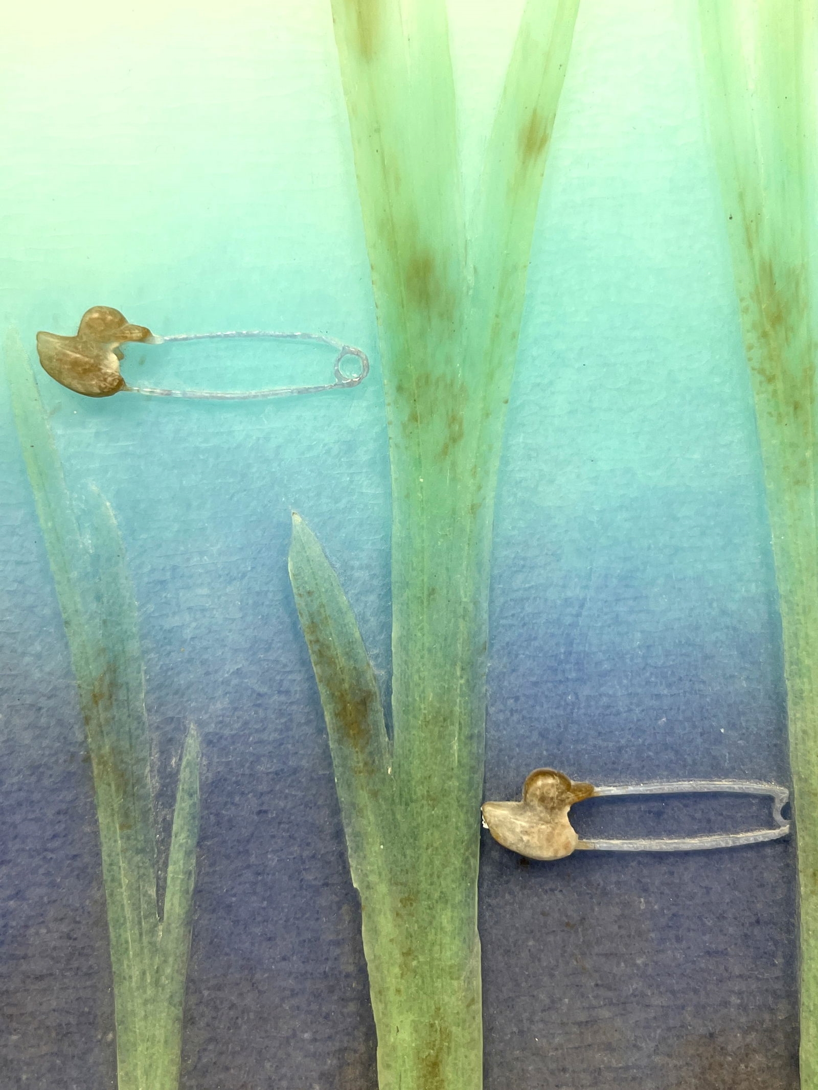 A vertical mixed-media artwork featuring tall green blades and scattered safety pins against a blue gradient background.