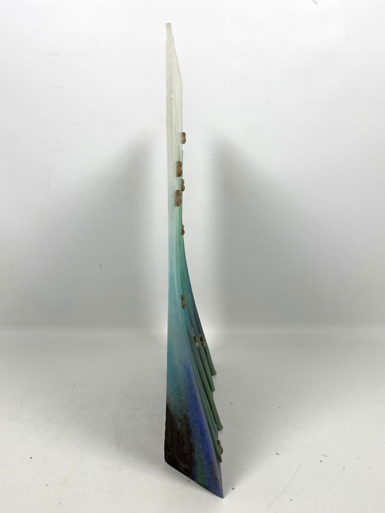 A vertical mixed-media artwork featuring tall green blades and scattered safety pins against a blue gradient background.