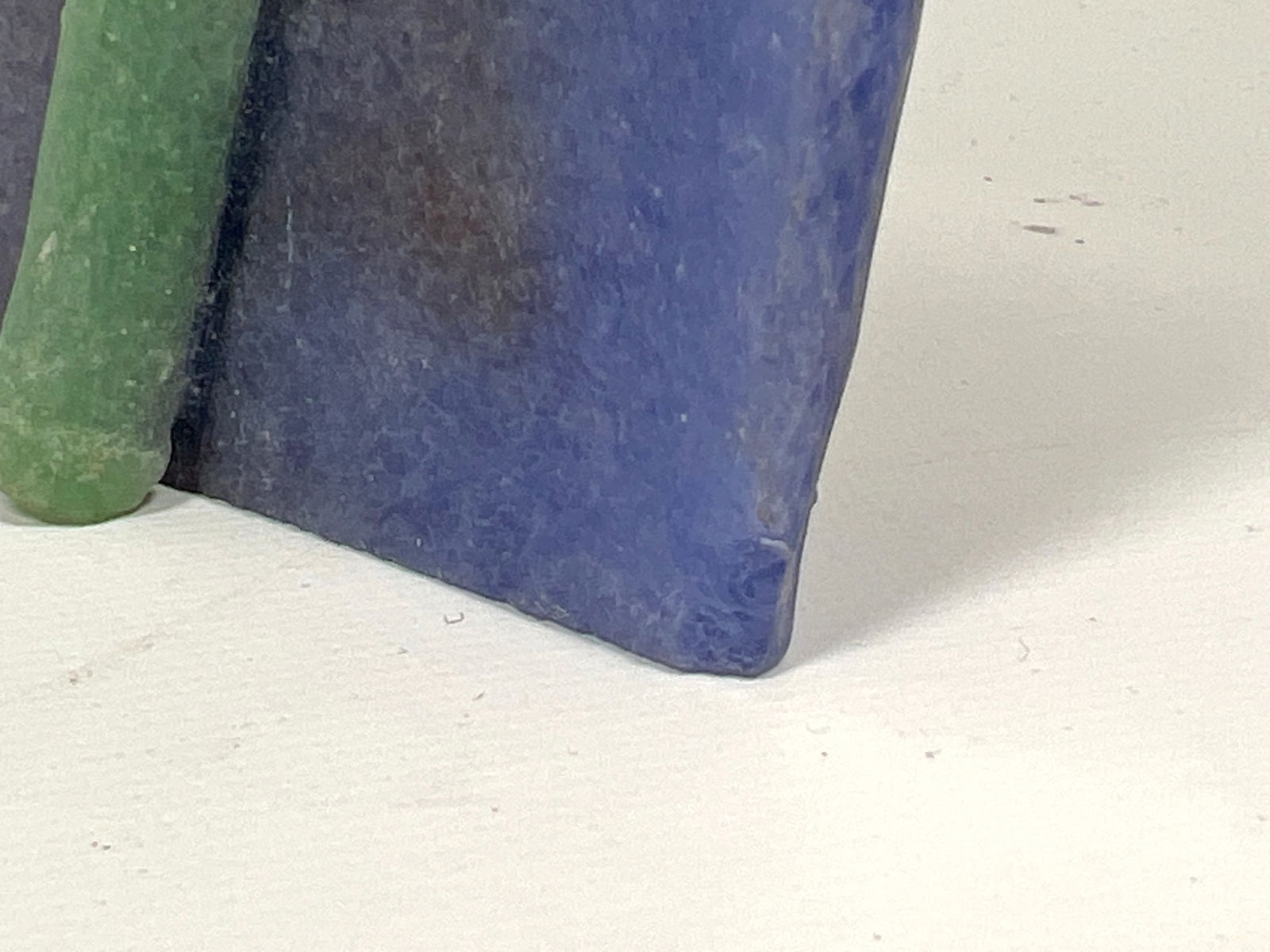 A vertical mixed-media artwork featuring tall green blades and scattered safety pins against a blue gradient background.